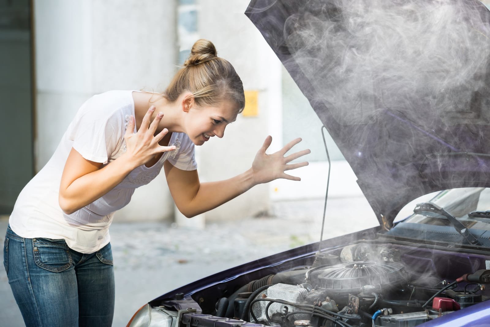 76263844_frustrated-woman-looking-at-broken-down-car-engine
